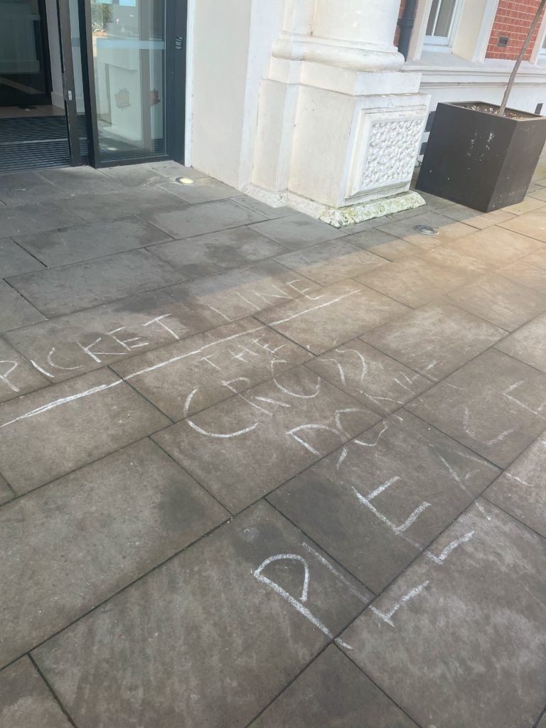 大学の本館に入るドアの前の地面に書かれたピケットラインを示す文字。恐らく"PICKET LINE" "DON'T CROSS"と書かれているが、正確に読み取れない。